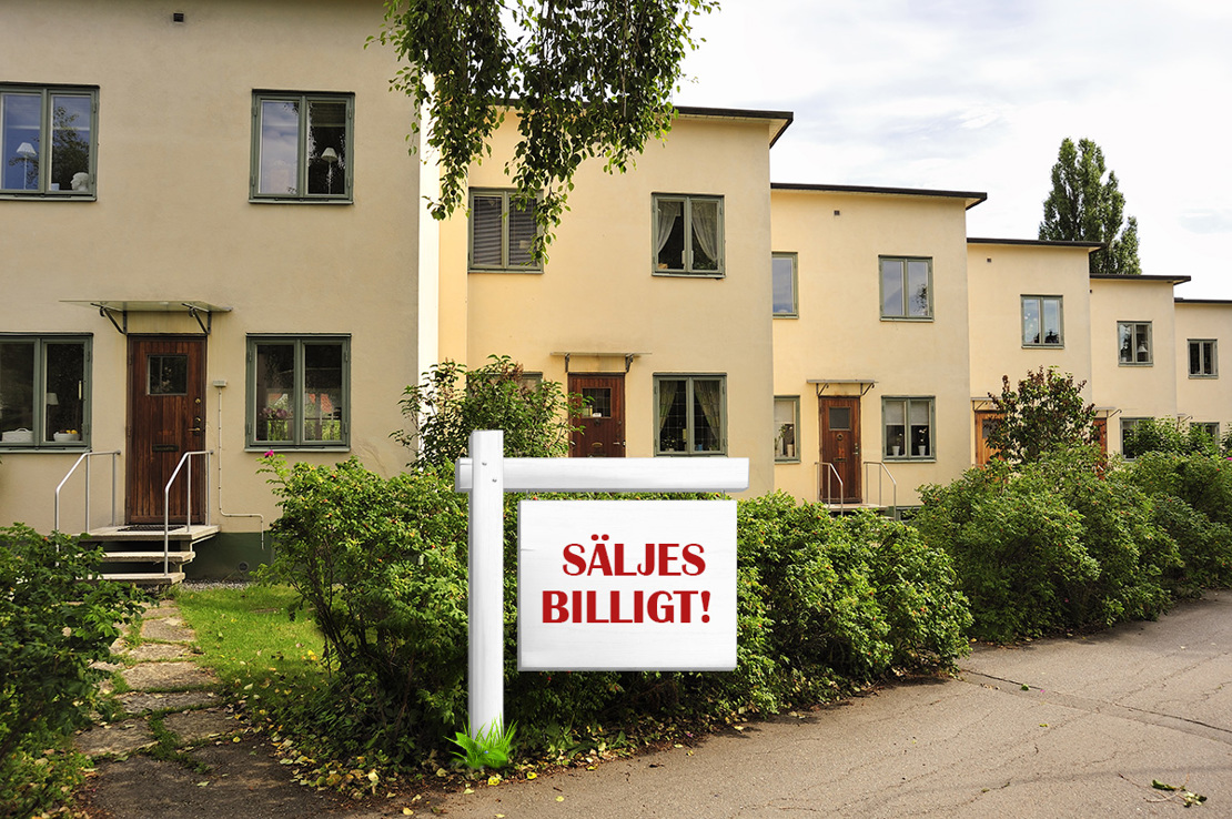 Skylt med texten Säljes billigt som står framför en rad med flerfamiljshus längs en gata.