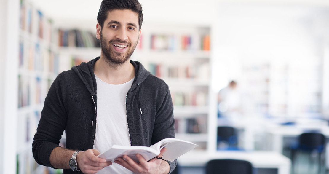 En student står i ett bibliotek och bläddrar i en bok.