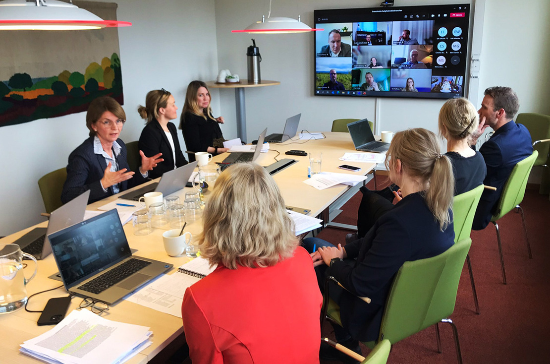 FMI:s medarbetare i ett konferensrum med en tv-skärm som visar ett onlinemöte med representanter från mäklarbranschen.